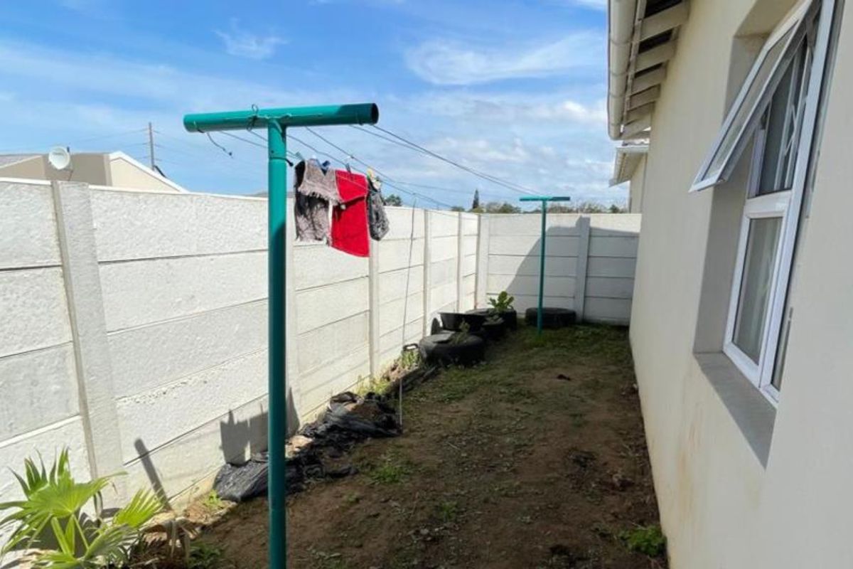 A side yard area featuring a precast concrete boundary wall, metal washing line, and access to the home via a casement window.