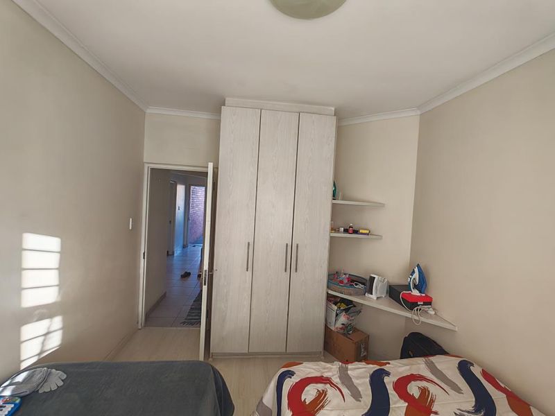 A standard bedroom featuring a window with fitted burglar bars and neutral wall finishes.