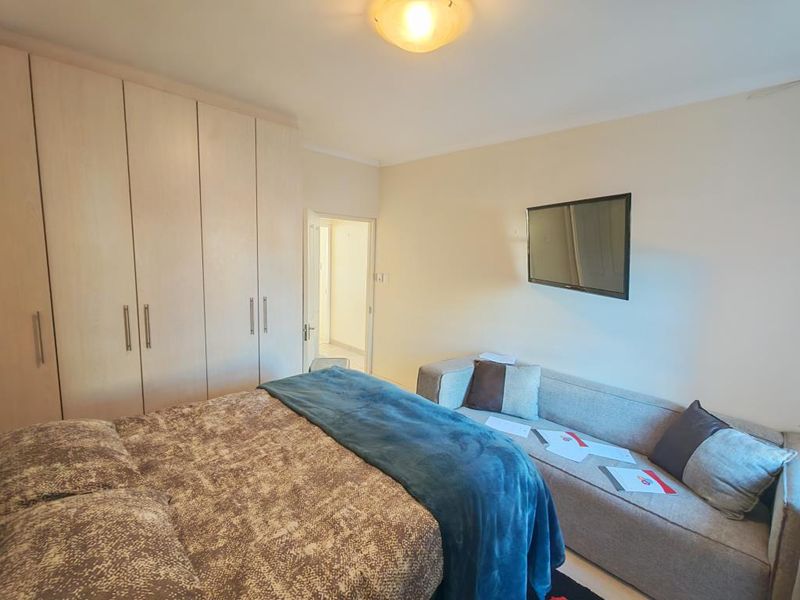 A cozy bedroom featuring neutral wall tones, a window with natural light, and a built-in wardrobe for storage.