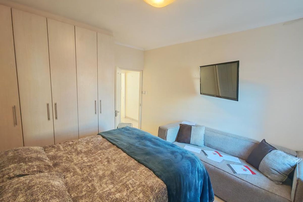 A cozy bedroom featuring neutral wall tones, a window with natural light, and a built-in wardrobe for storage.