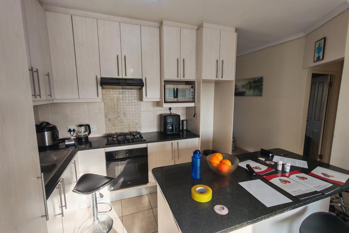 A functional kitchen featuring light-toned cabinetry, granite countertops, a breakfast bar, and tiled flooring, with direct access to an exterior doorway.
