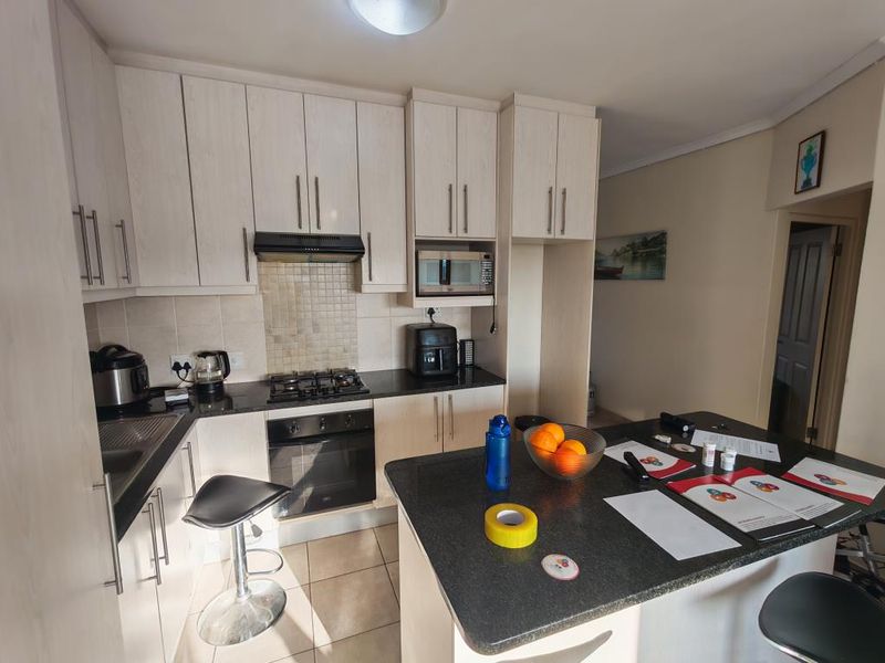 A functional kitchen featuring light-toned cabinetry, granite countertops, a breakfast bar, and tiled flooring, with direct access to an exterior doorway.