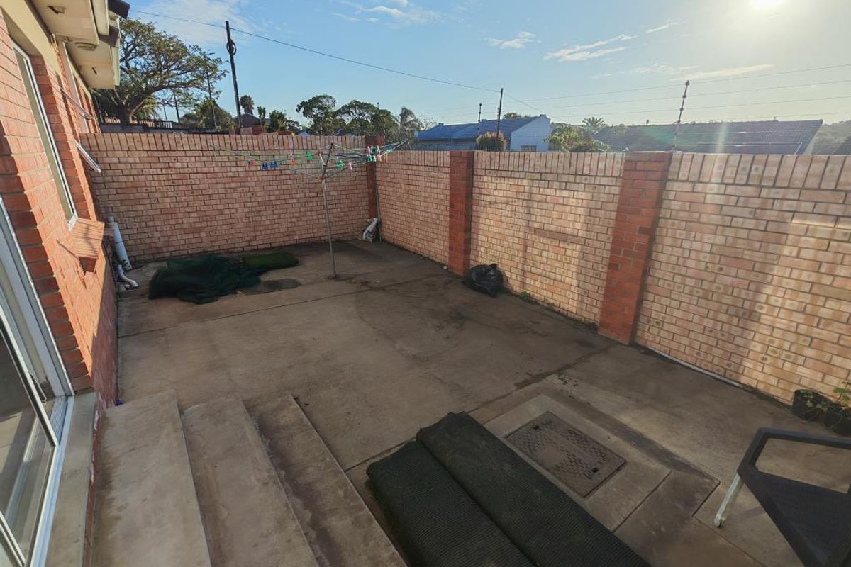 A private rear courtyard featuring a concrete patio, brick boundary walls, and direct access to the townhouse interior through sliding doors.
