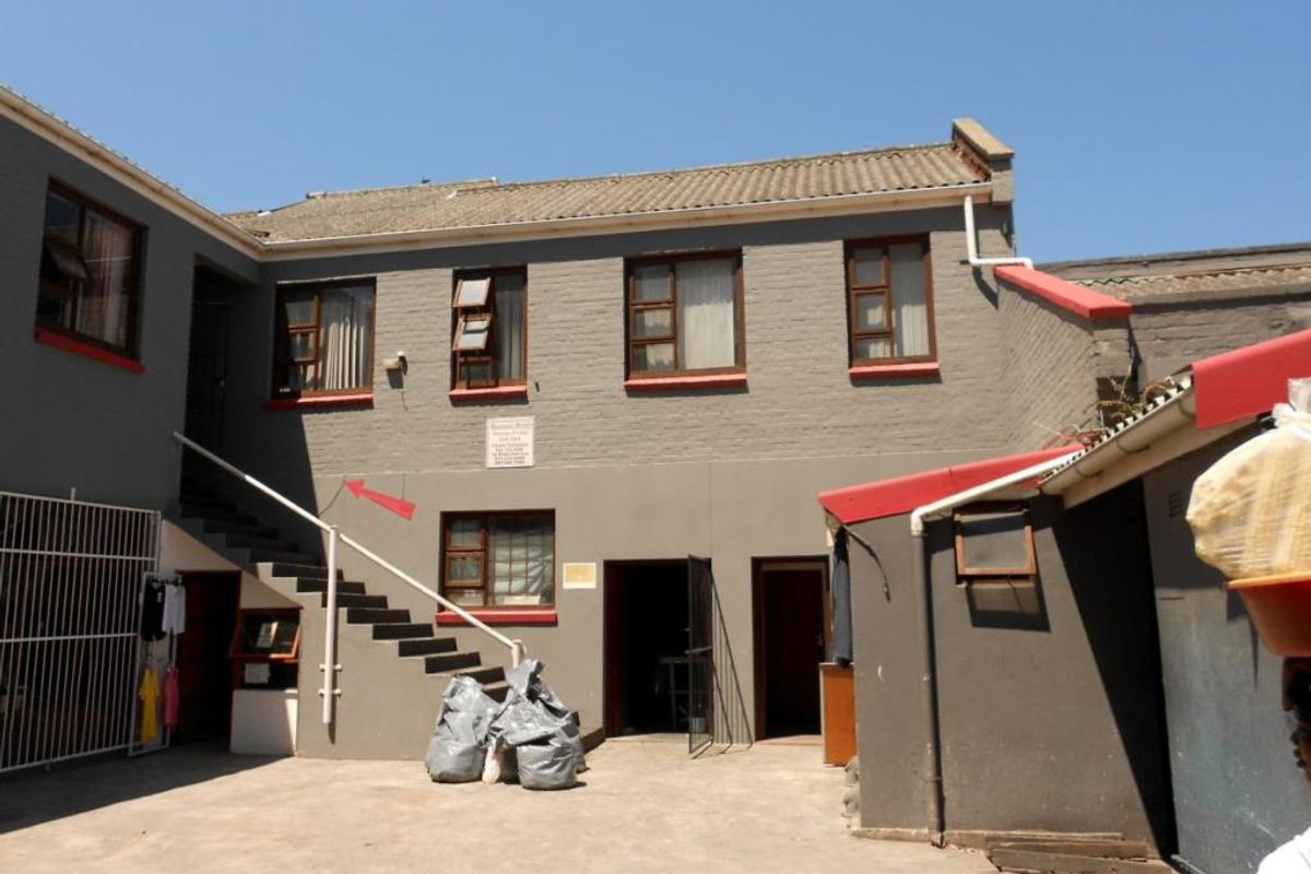 Rear exterior view of a commercial building featuring a concrete staircase, painted brick facade, and tiled roofing.