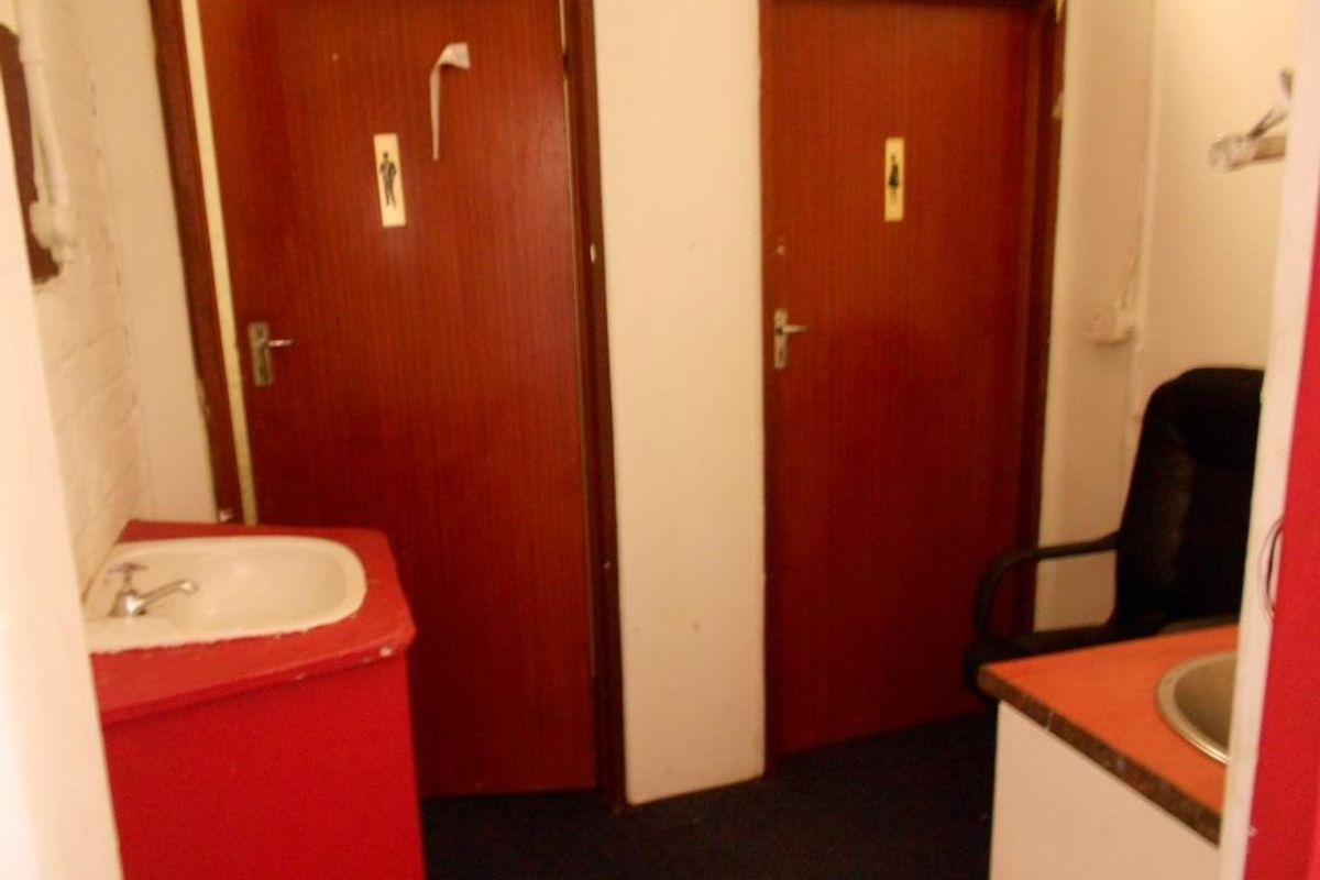 A functional commercial restroom area featuring dual access doors, vanity units with integrated washbasins, and dated interior finishes.