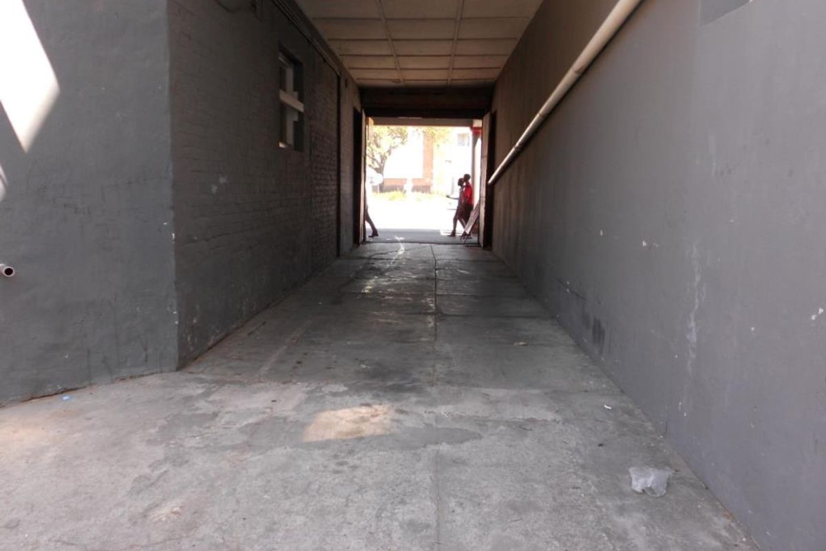 A covered utility corridor or passageway featuring concrete flooring and painted masonry walls, providing access between building sections.