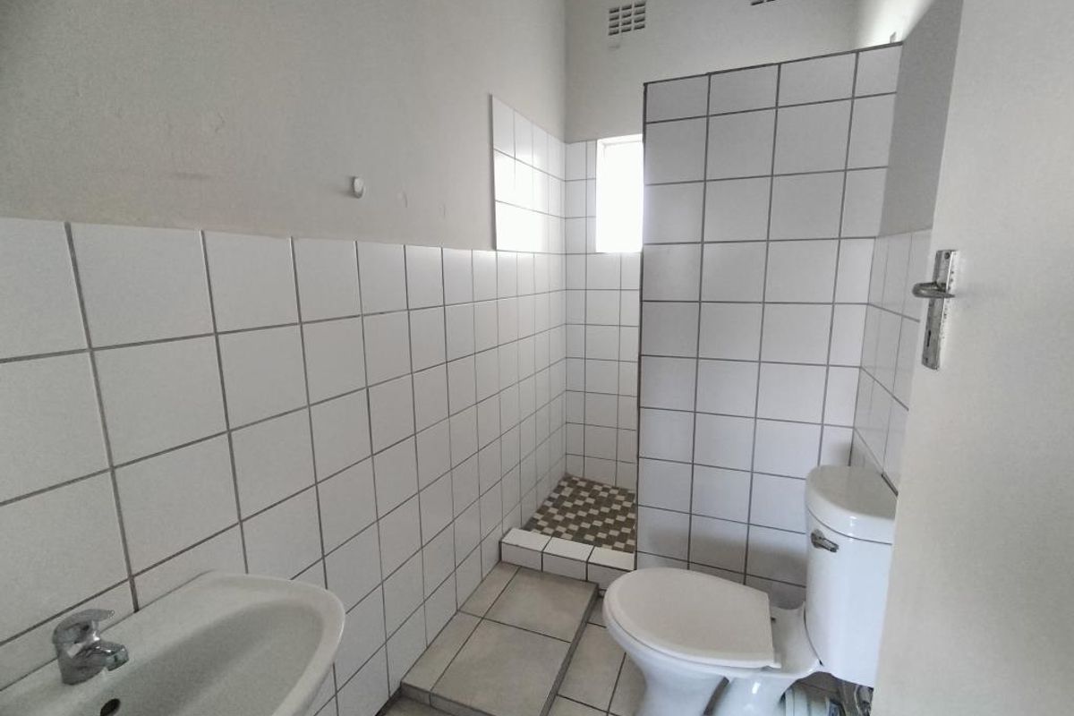 A functional bathroom featuring a walk-in shower enclosure, a standard toilet, and a wall-mounted basin with white tiled walls and flooring.