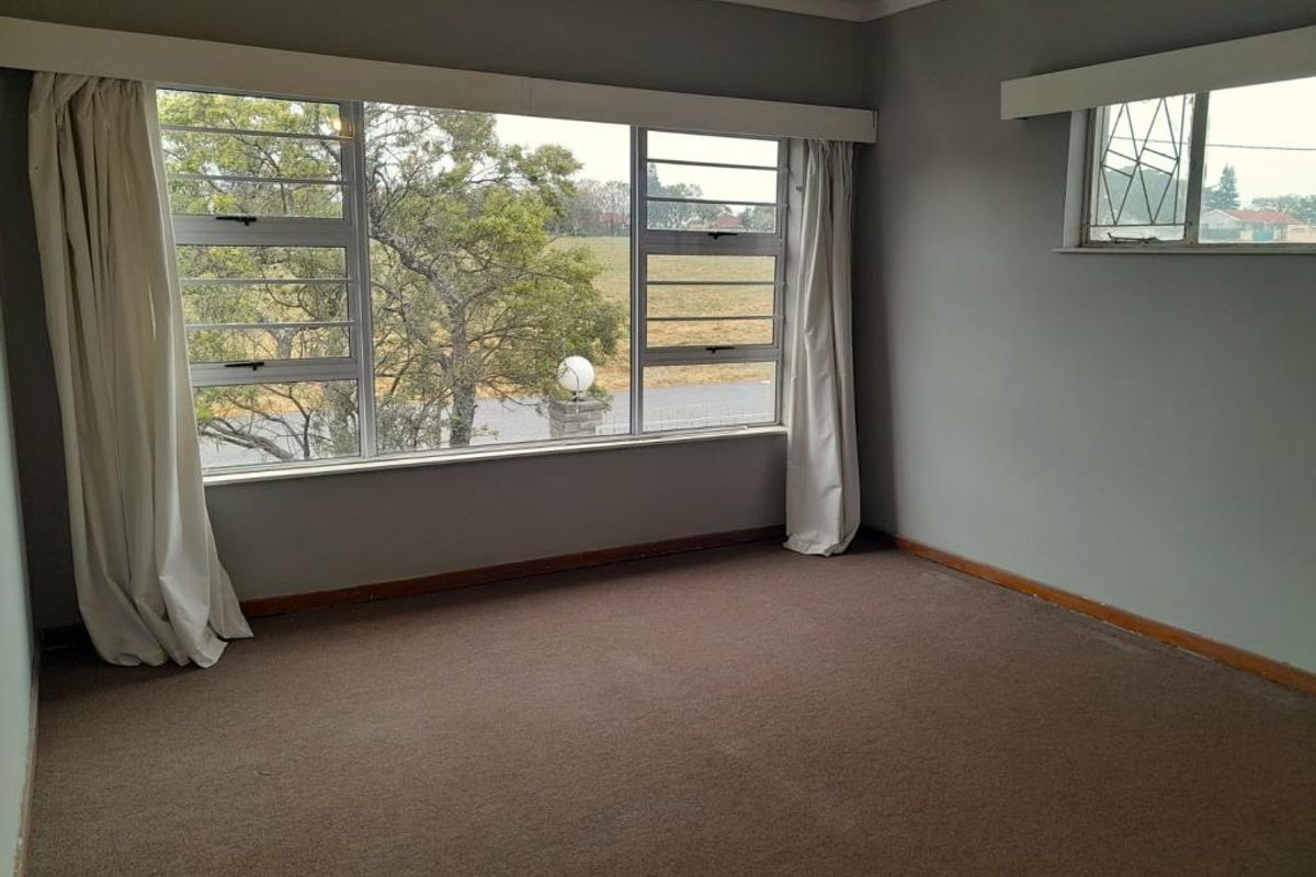 A spacious, empty bedroom featuring large windows with natural light, neutral wall tones, and fitted carpeting.