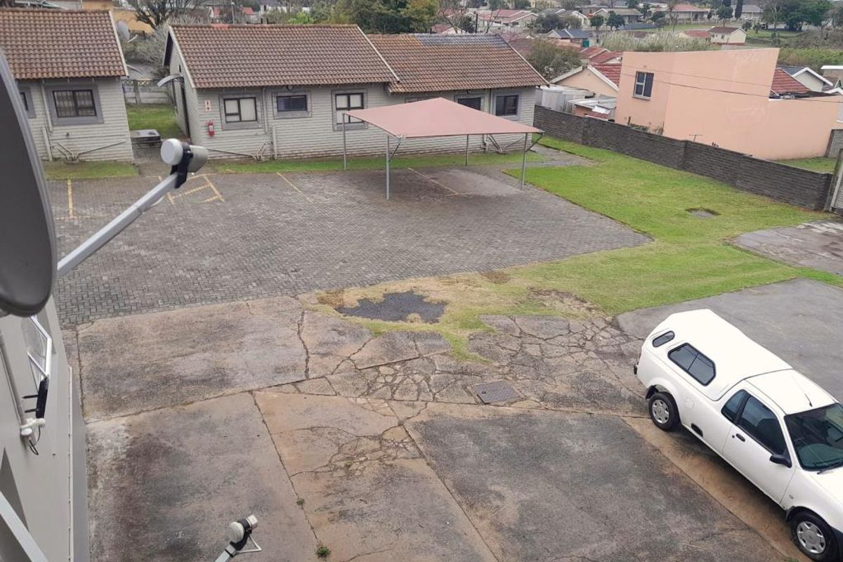 Elevated view of the apartment complex parking area featuring paved bays, a covered carport structure, and surrounding communal grounds.