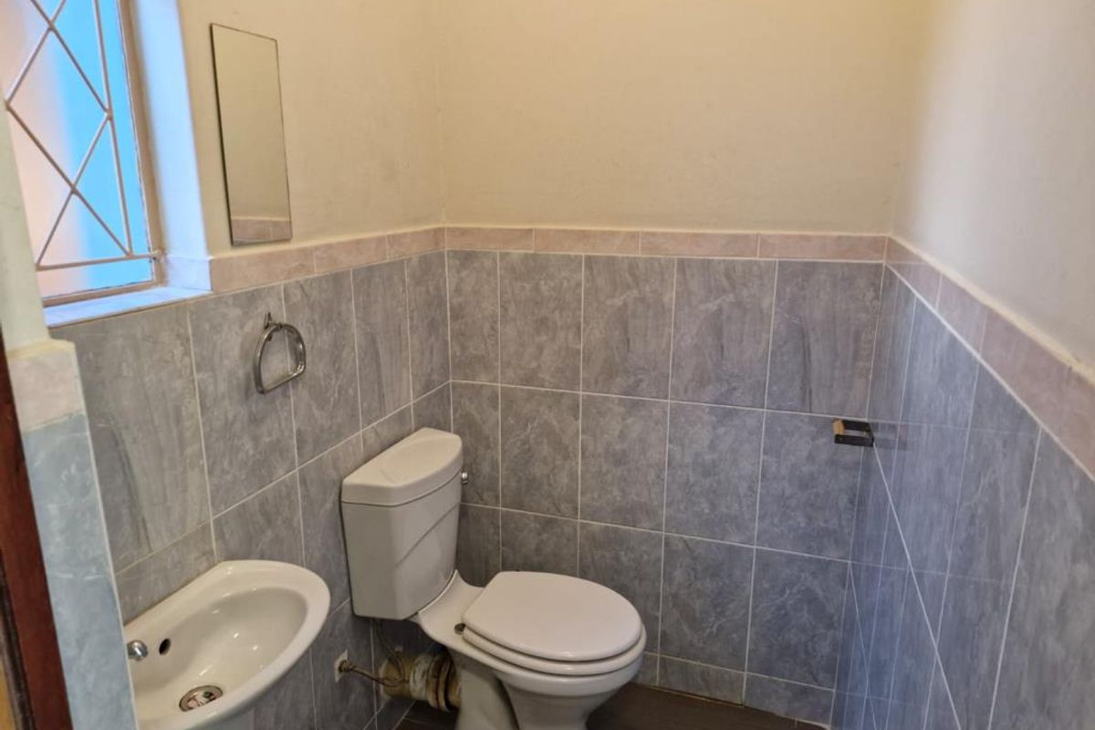 A compact guest bathroom featuring a pedestal basin, a standard toilet, and partial wall tiling with a window for natural light.