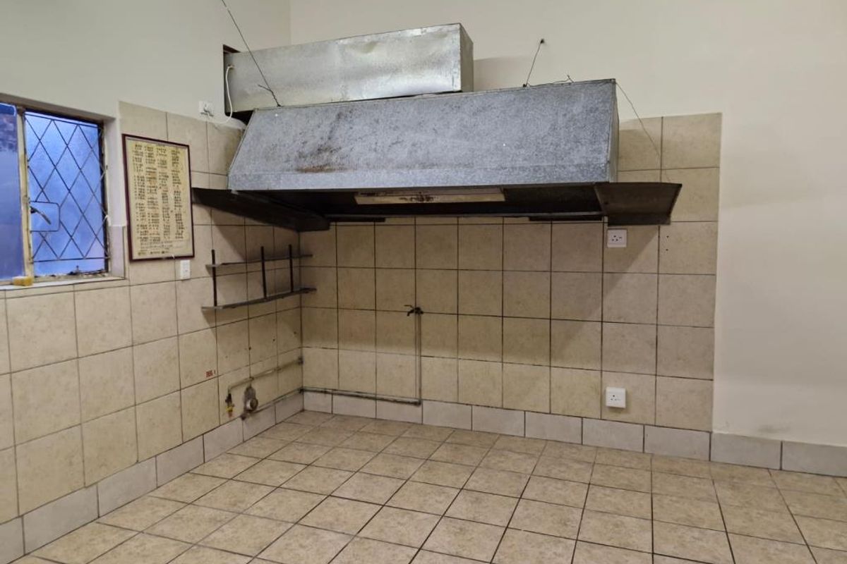 Commercial kitchen area featuring a large industrial extractor hood, tiled walls, and tiled flooring, ready for equipment installation.