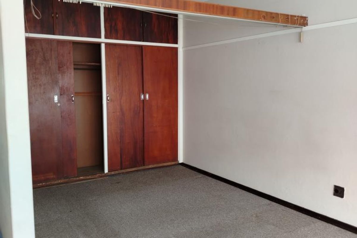 A bedroom featuring dated built-in wooden wardrobes, carpeted flooring, and a neutral wall finish, offering a blank canvas for renovation.
