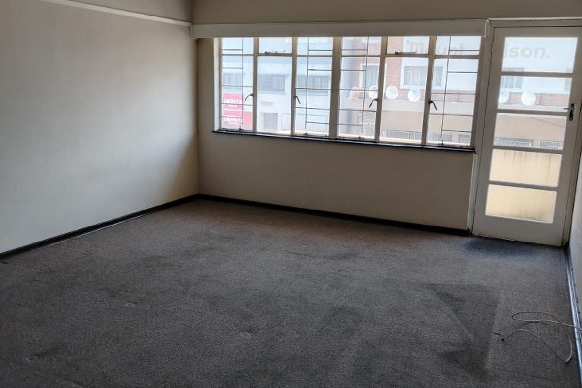 An empty living room featuring carpeted flooring, large windows, and a glass-paneled door leading to an outdoor area.
