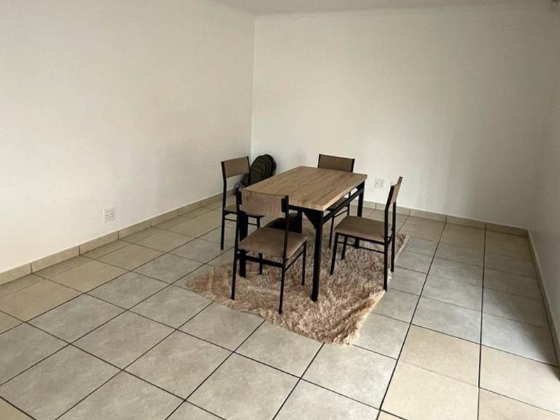 A simple dining area featuring neutral tiled flooring and plain white walls, providing a functional space for meals.