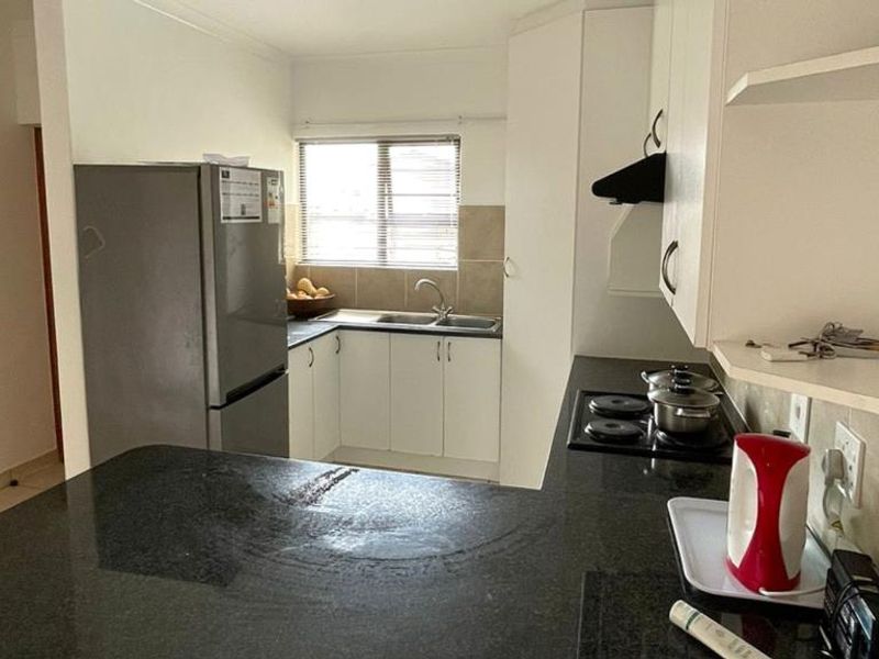 A functional kitchen featuring built-in cabinetry, dark granite countertops, a tiled backsplash, and a built-in hob with an extractor fan.