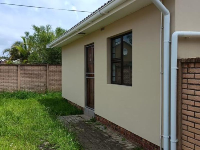 Rear exterior view of the apartment featuring a paved walkway, brick boundary wall, and functional guttering system.