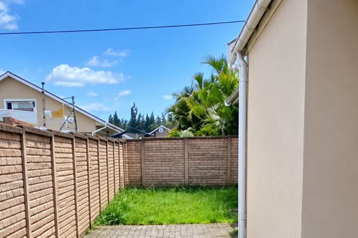 A private rear garden featuring a paved patio area, a small lawn, and secure brick boundary walls.