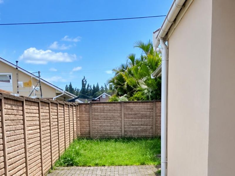 A private rear garden featuring a paved patio area, a small lawn, and secure brick boundary walls.