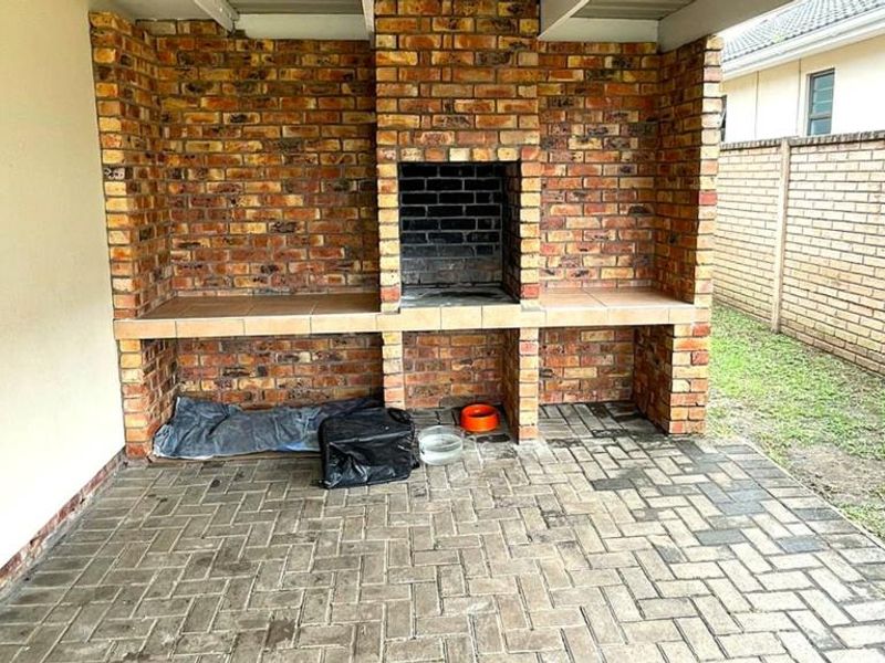 Covered outdoor patio area featuring a substantial built-in brick braai with tiled prep surfaces and durable paved flooring.