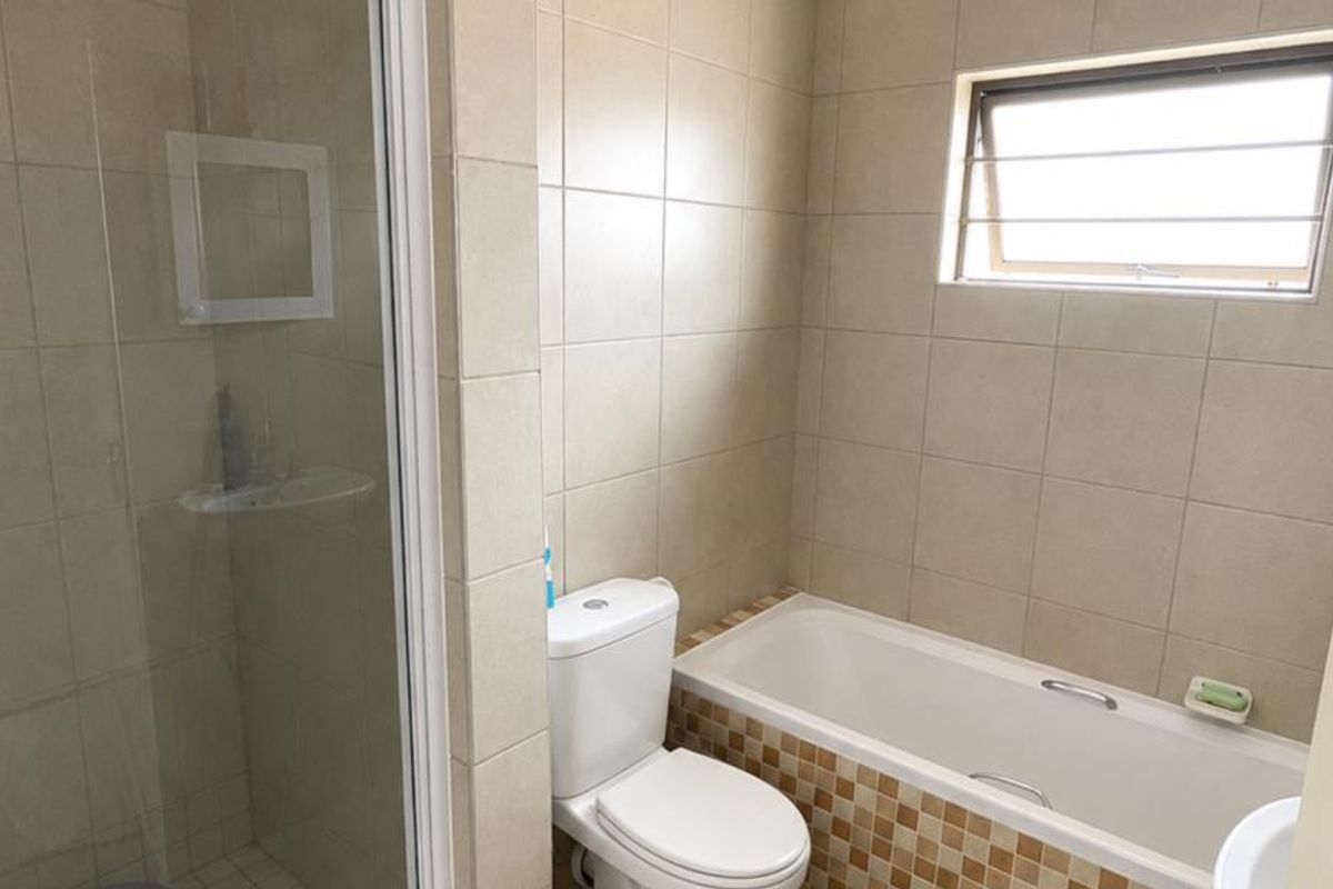 A functional bathroom featuring a separate shower enclosure, a bathtub with a tiled apron, and a toilet, finished with neutral wall tiling.