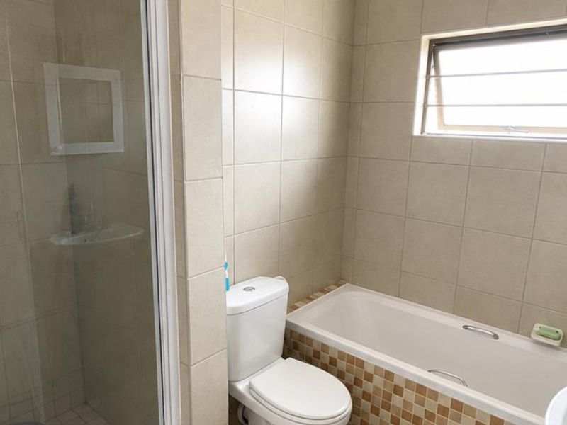 A functional bathroom featuring a separate shower enclosure, a bathtub with a tiled apron, and a toilet, finished with neutral wall tiling.