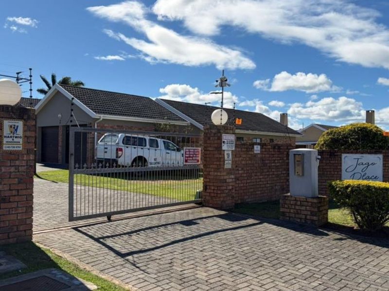 Front entrance view of the townhouse complex featuring a secure gated access, brick boundary walls, electric fencing, and a paved driveway.