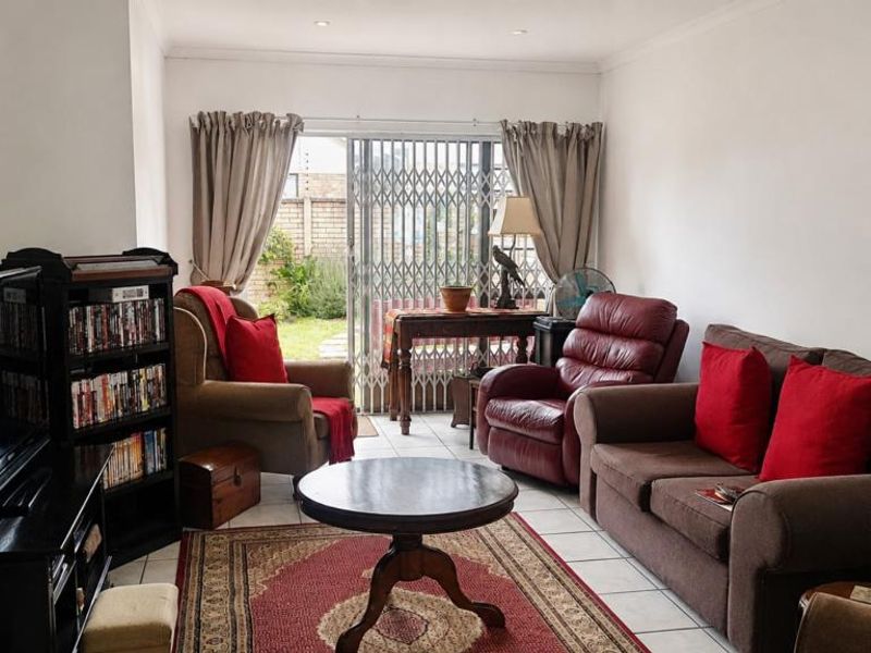 A comfortable living room featuring tiled flooring, recessed downlighting, and a sliding glass door providing access to the rear garden area.