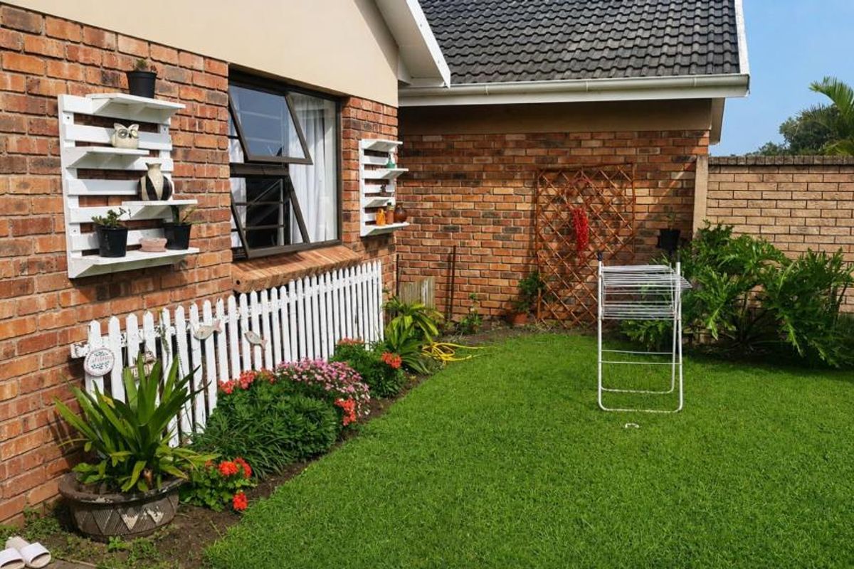A well-maintained rear garden area featuring face brick exterior walls, a tiled roof, and a neat lawn with established garden beds.