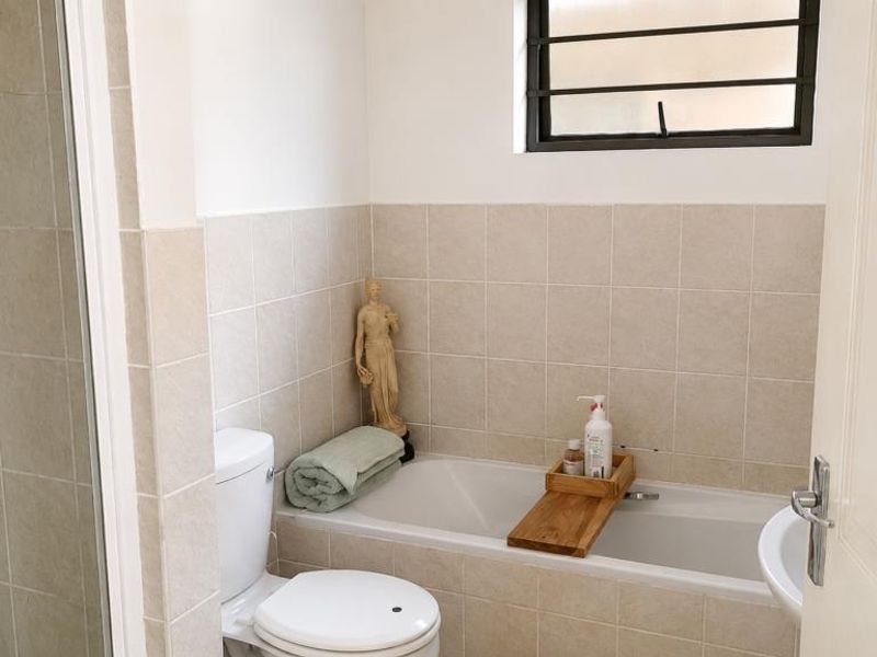 A functional bathroom featuring a built-in bathtub, toilet, and tiled wall finishes, complemented by a window with security bars.