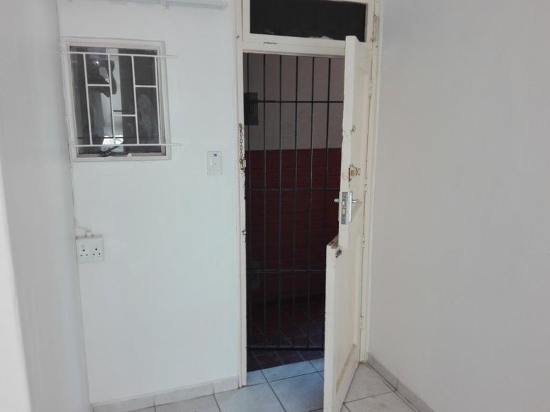 An interior entry area featuring tiled flooring, a security gate, and a window with security bars, showing signs of wear and tear.