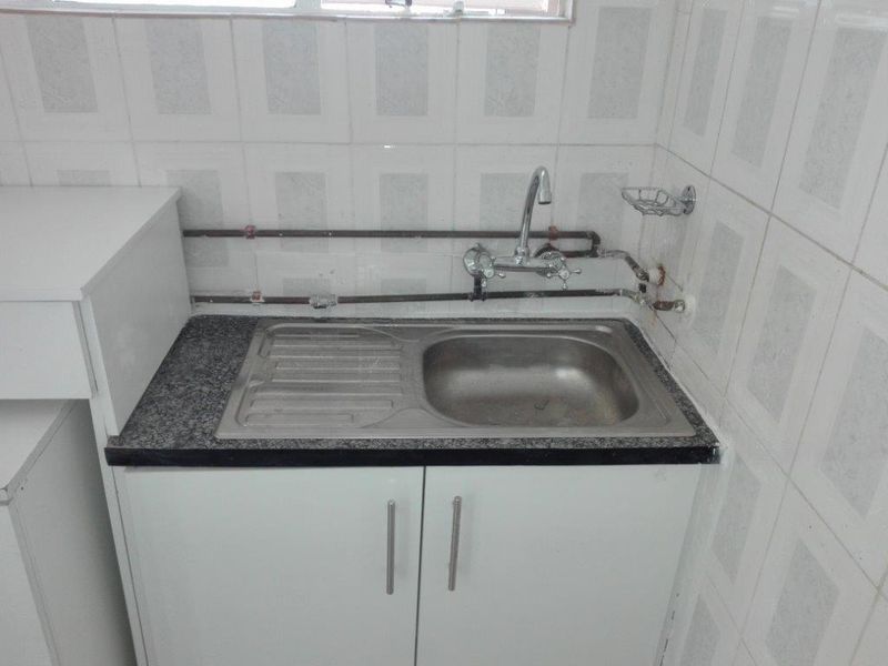 A functional scullery area featuring a stainless steel sink, granite countertop, and tiled splashback with exposed plumbing fixtures.