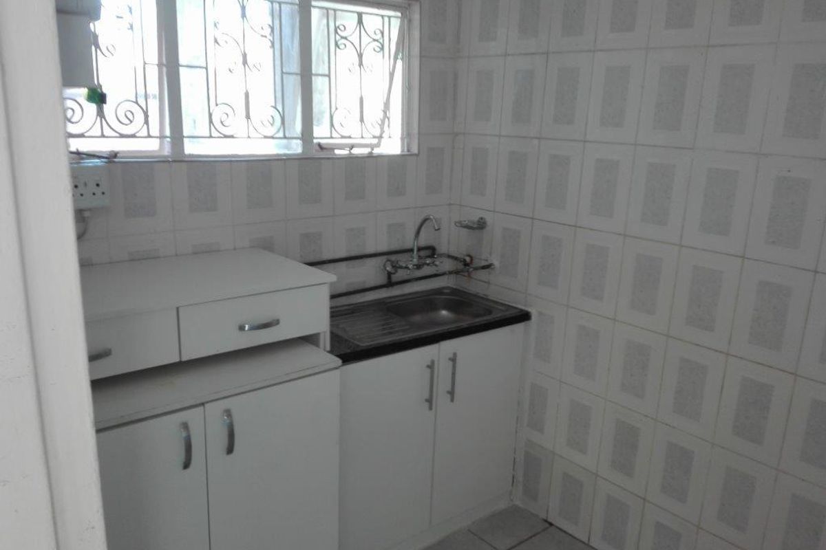 A compact, functional kitchen featuring built-in white cabinetry, a stainless steel sink, and full-height wall tiling, ready for a modern update.