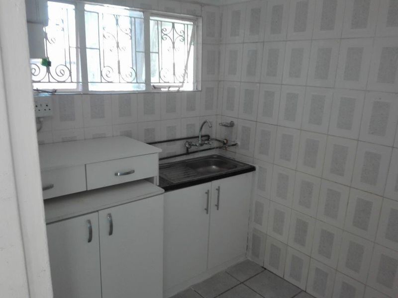 A compact, functional kitchen featuring built-in white cabinetry, a stainless steel sink, and full-height wall tiling, ready for a modern update.