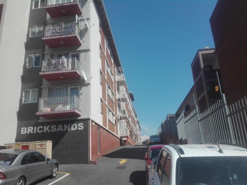Exterior view of the Bricksands apartment complex, featuring a multi-story brick building with private balconies and a paved driveway entrance.