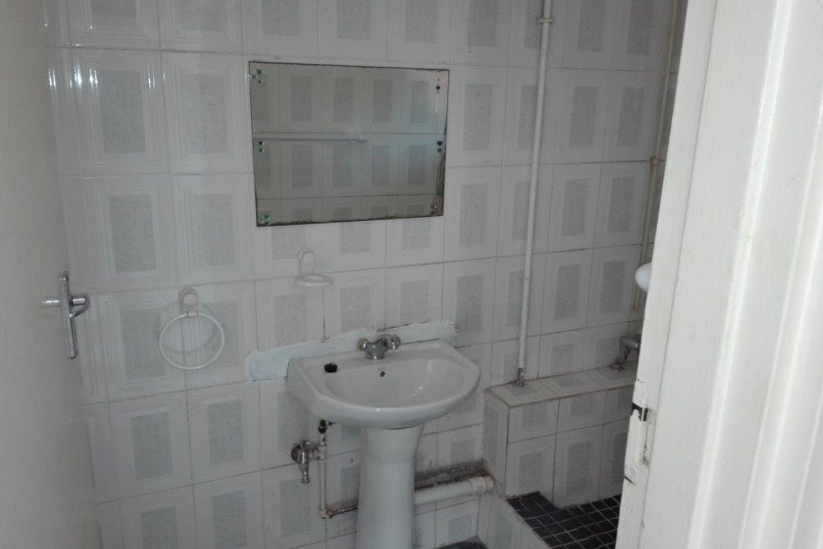 A small, dated bathroom featuring a pedestal basin, wall-mounted mirror, and fully tiled walls. The space requires modernization and cosmetic updates.