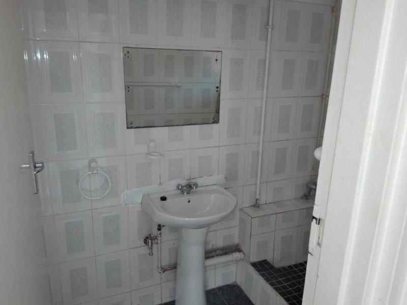 A small, dated bathroom featuring a pedestal basin, wall-mounted mirror, and fully tiled walls. The space requires modernization and cosmetic updates.