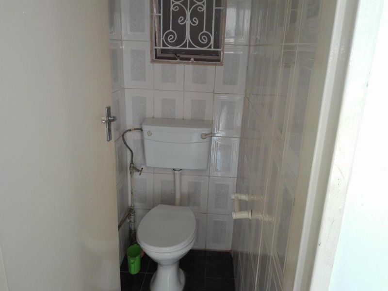 A compact bathroom featuring ceramic wall and floor tiles, a standard toilet with a high-level cistern, and a small window with a security grille.