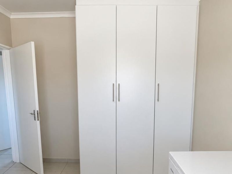 A clean, neutral bedroom featuring a large white built-in wardrobe and coved ceilings, offering a bright and functional space.