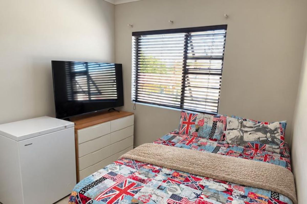 A functional bedroom featuring neutral wall tones, a window with fitted venetian blinds, and coving detail.