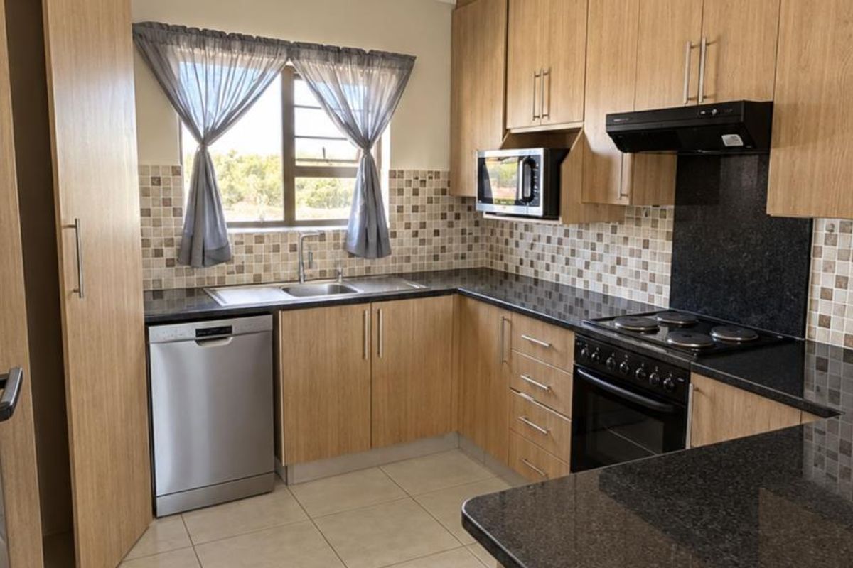 A well-maintained kitchen featuring light wood-finish cabinetry, dark granite countertops, mosaic tile backsplash, and integrated appliances including an oven, hob, and extractor fan.