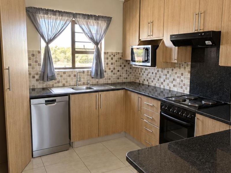 A well-maintained kitchen featuring light wood-finish cabinetry, dark granite countertops, mosaic tile backsplash, and integrated appliances including an oven, hob, and extractor fan.