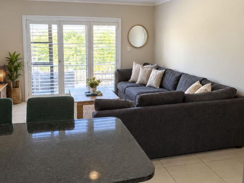 Open-plan living area featuring tiled floors, granite kitchen counter, and french doors leading to an outdoor space with security shutters.