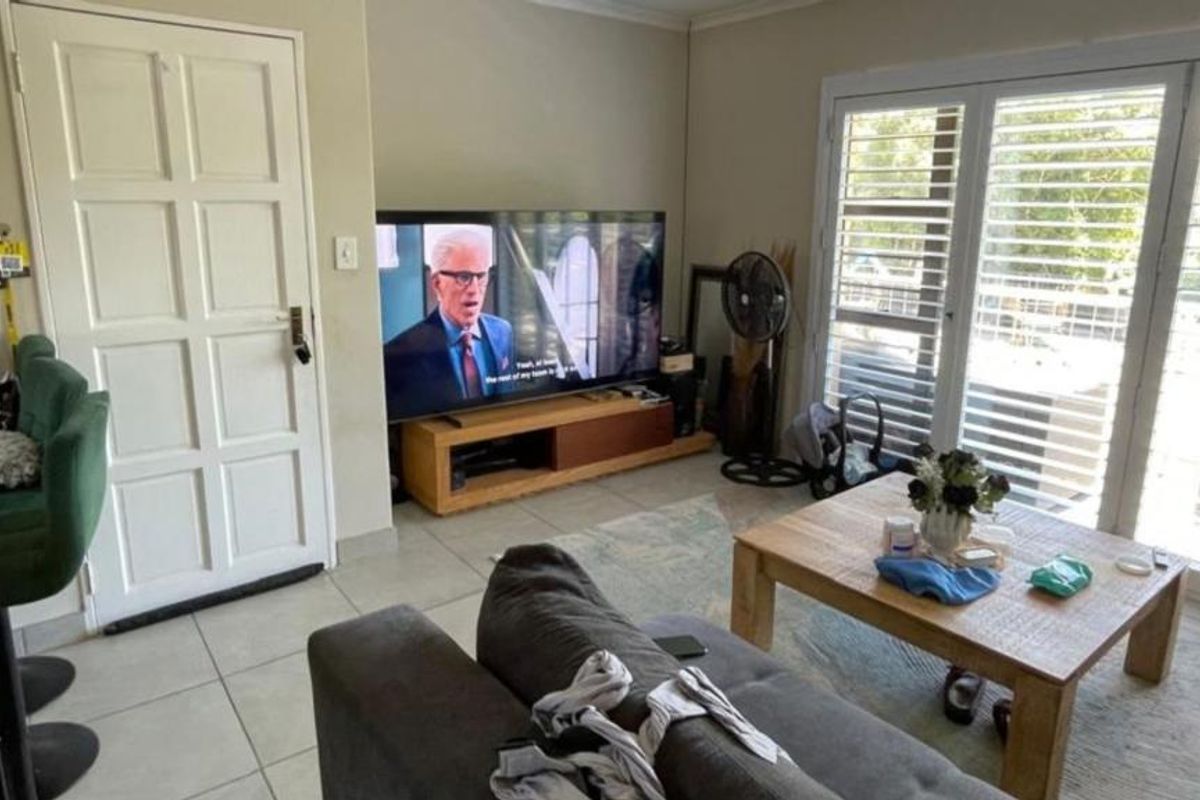 A living room featuring tiled flooring, a panel door, and french doors with security shutters leading to an outdoor area.