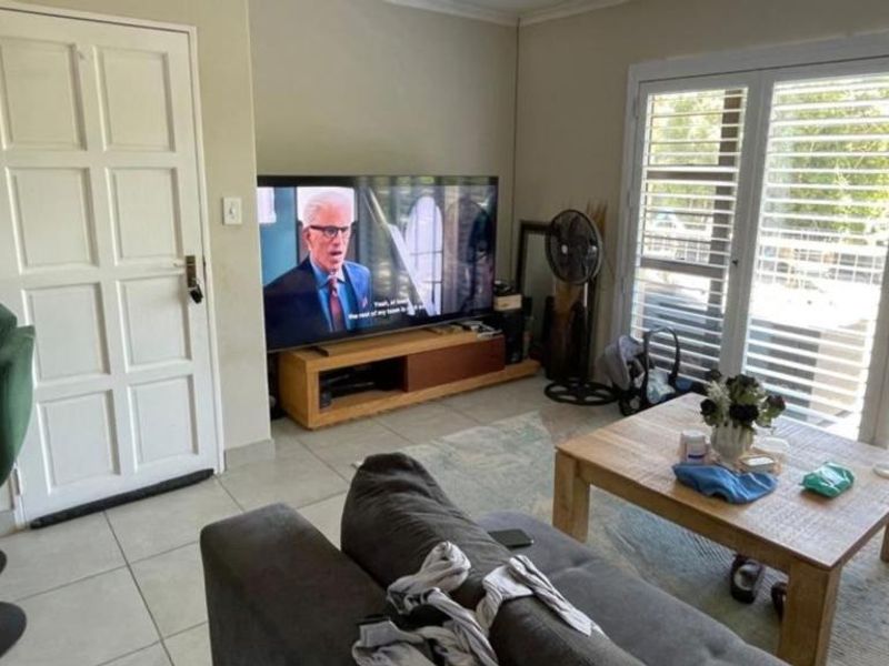 A living room featuring tiled flooring, a panel door, and french doors with security shutters leading to an outdoor area.