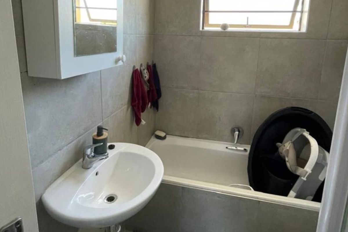 Compact bathroom featuring a pedestal basin, bathtub with mixer tap, and neutral wall tiling.
