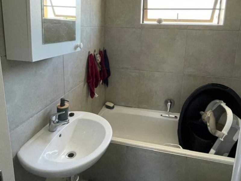Compact bathroom featuring a pedestal basin, bathtub with mixer tap, and neutral wall tiling.