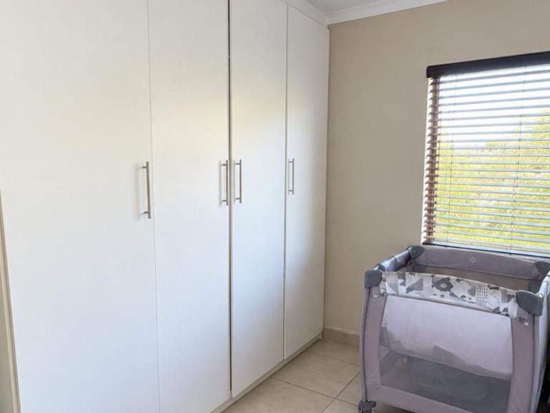 A bright bedroom featuring floor-to-ceiling built-in cupboards, tiled flooring, and large windows fitted with venetian blinds.
