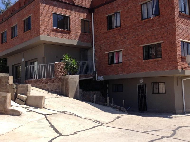 Exterior view of a multi-story brick apartment building featuring a concrete driveway with significant surface cracking and structural wear.