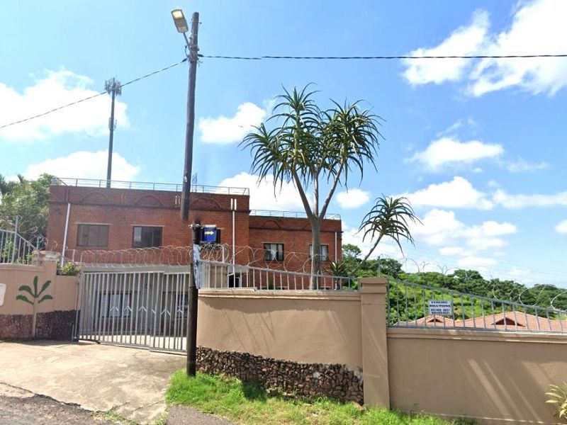 Exterior view of the property featuring a brick facade, secure perimeter wall with razor wire, and gated driveway entrance.
