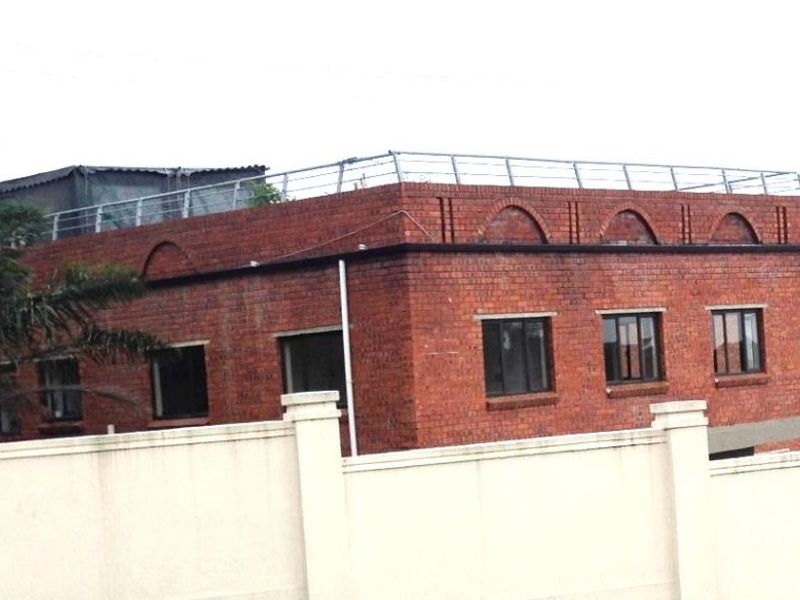 Exterior view of a multi-story brick apartment building featuring arched architectural detailing and a rooftop terrace with metal safety railings.